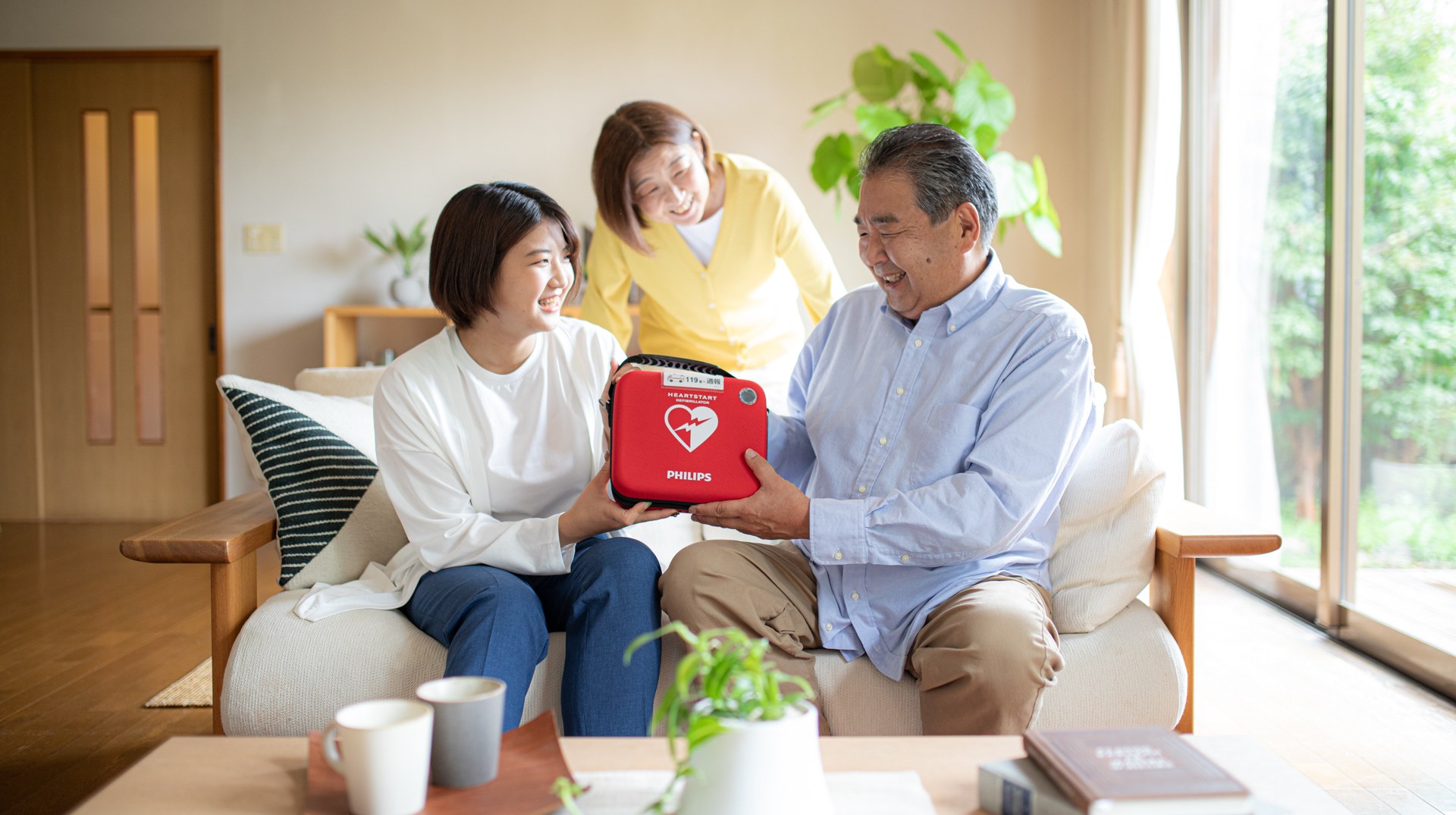 自宅のリビングで家庭用AED ハートスタート HS1 Home を手にする家族